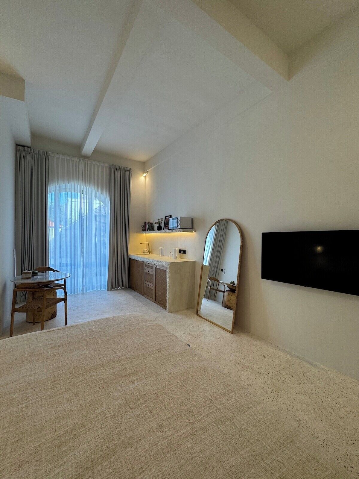 A hotel room with a bed, a desk, a chair, a TV, a mirror, and a window with curtains.