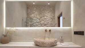 A bathroom with a stone wall, a round sink, and a mirror above it. - Brand New Apartments in Sanur+500m to Ocean+Pool (Kota Denpasar)