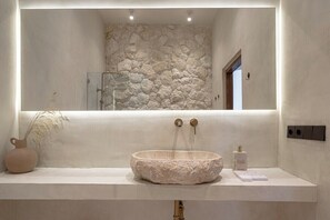 A bathroom with a stone wall, a round sink, and a mirror above it. - Brand New Apartments in Sanur+500m to Ocean+Pool (Kota Denpasar)