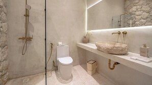 Ein modernes Badezimmer mit Steinwand, freistehender Toilette, Waschbecken auf Säule und einer Duschkabine aus Glas.