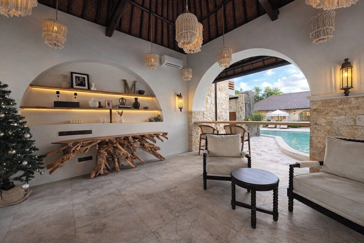 A cozy indoor seating area with a stone fireplace, a wooden coffee table, and a view of a pool.