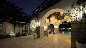Ein Terrassenbereich im Freien mit Steinböden, einem Pool und Sitzgelegenheiten unter Bögen.