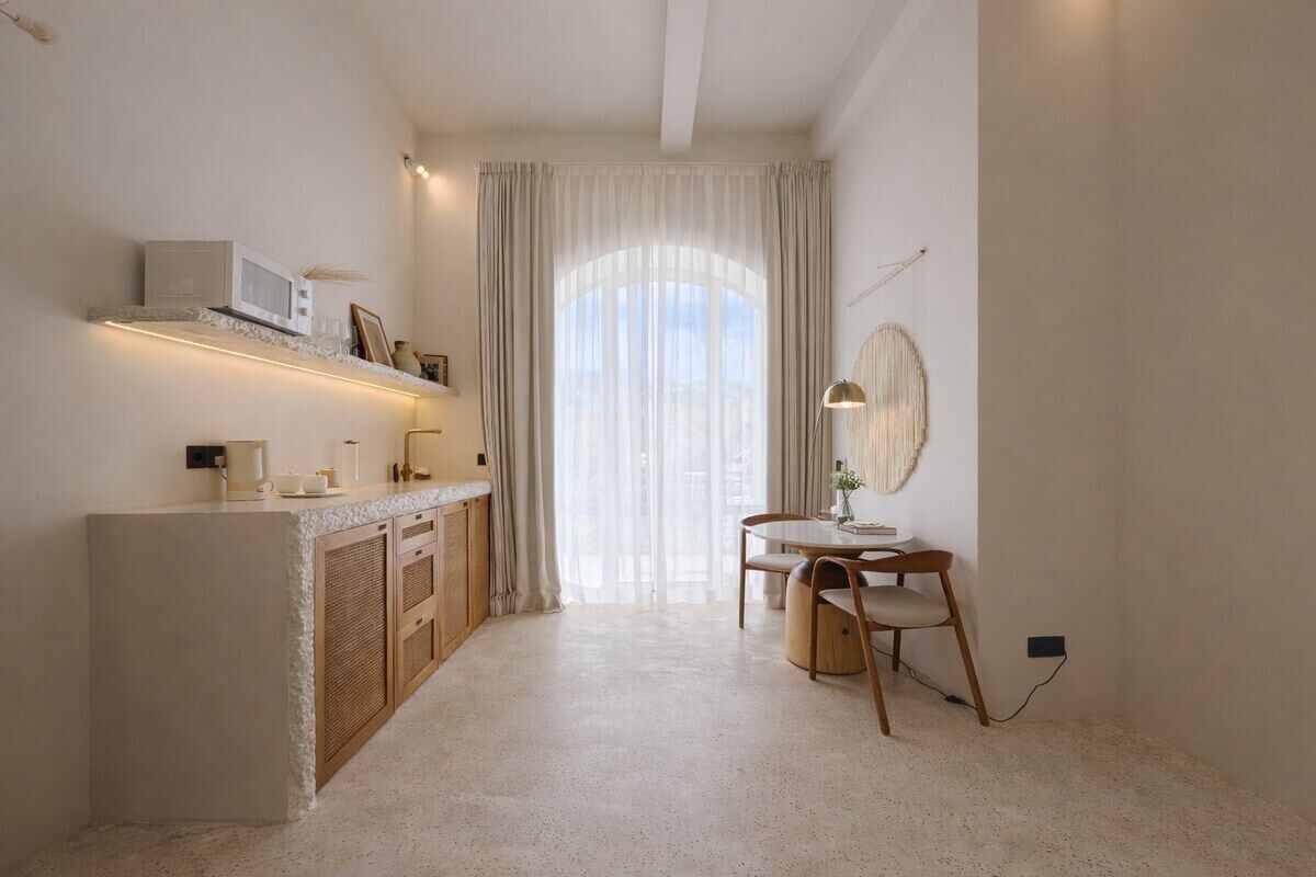 A minimalist room with a kitchenette, a dining area, and a large window with sheer curtains.