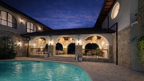 A swimming pool with a stone patio and outdoor seating area, surrounded by a building with arched windows and stone walls. - New Cozy 1BR Next to the Ocean w Pool+Patio+Garden (Kota Denpasar)
