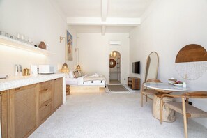 A modern, well-lit room with a bed, a dining table, and a kitchen area with a white countertop and wooden cabinets. - Serene 1BR Retreat Next to the Ocean w Pool+Patio (Denpasar Selatan)