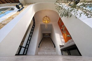 A modern interior with a staircase leading to a lower level, a decorative light fixture, and a wall with a colorful pattern. - Serene 1BR Retreat Next to the Ocean w Pool+Patio (Denpasar Selatan)