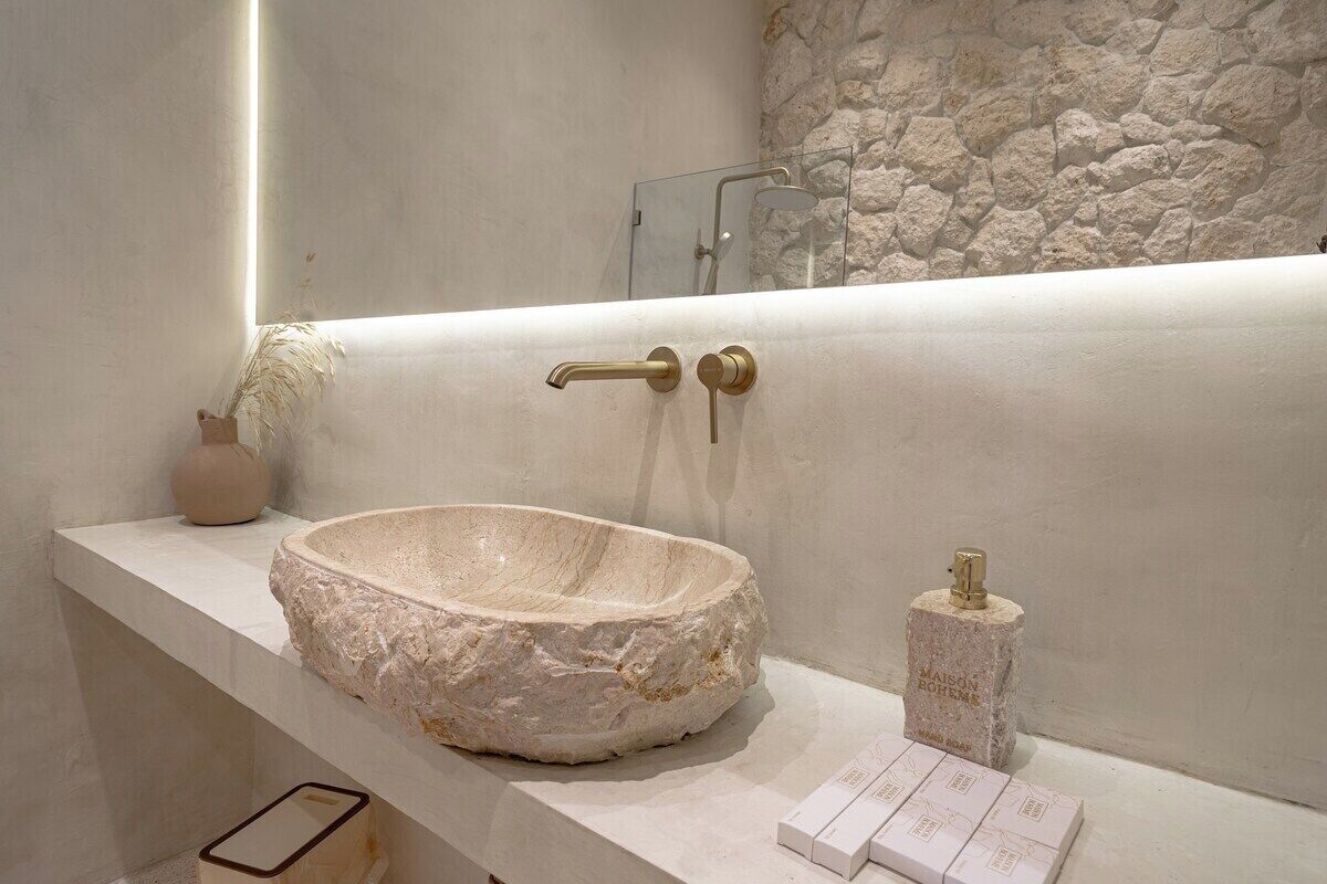 A bathroom with a stone sink, a handheld showerhead, and a bottle of soap.