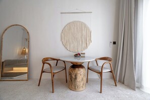 Ein Zimmer mit einem runden Tisch, zwei Stühlen, einer runden Wanddekoration, einem Spiegel und einem Fenster mit Vorhängen.