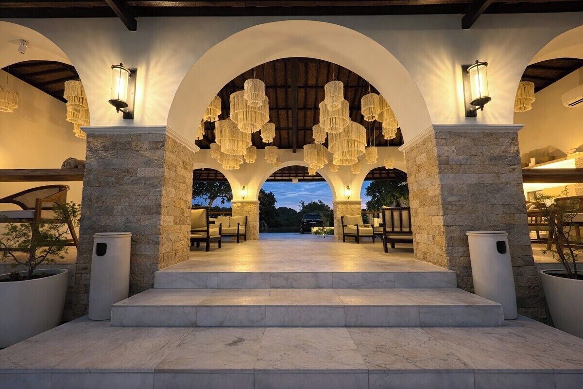 An outdoor covered area with stone pillars, a set of steps leading to a seating area, and hanging light fixtures.