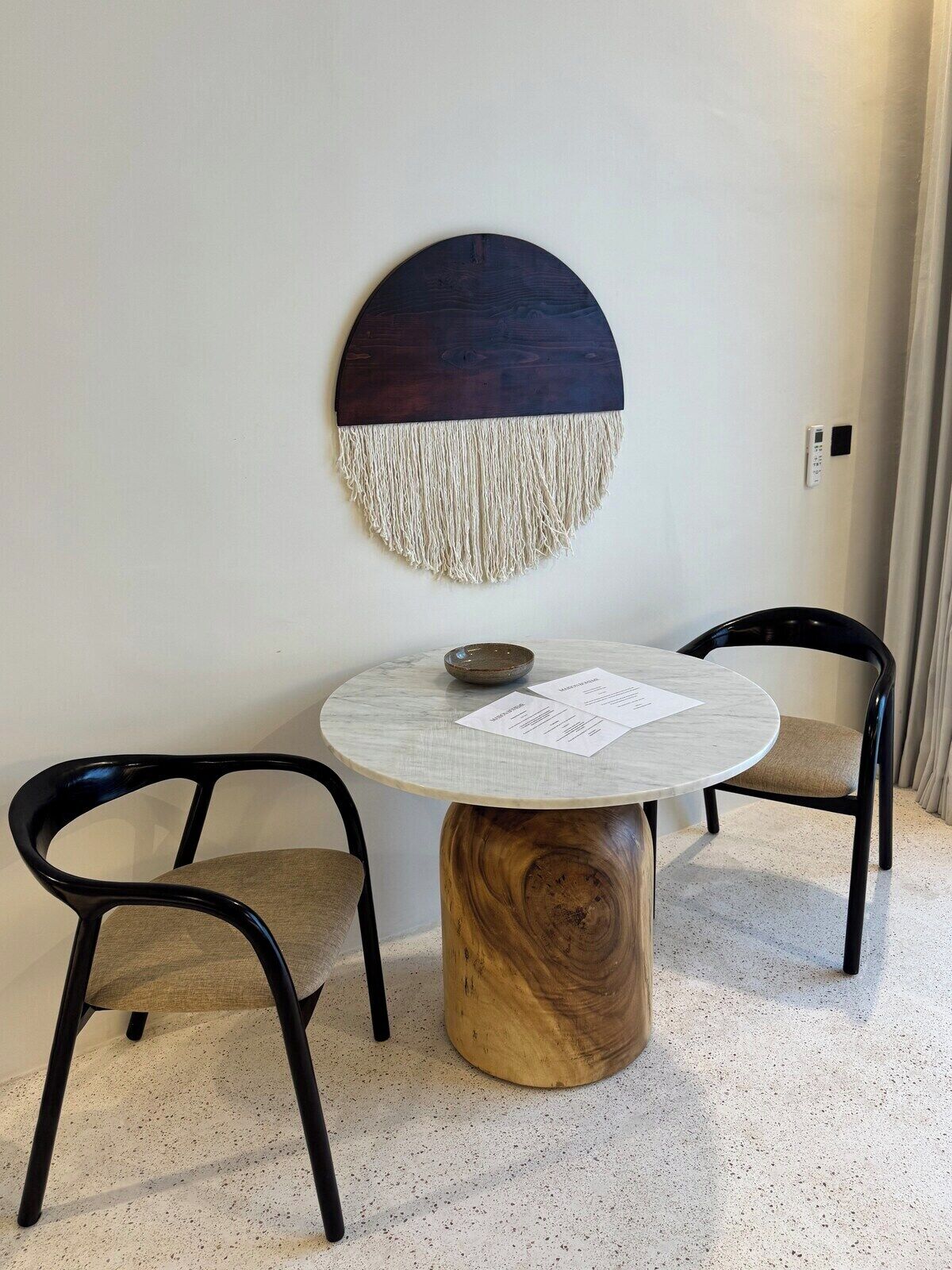 A round table with a wooden base, two black chairs, and a wall-mounted decorative piece.