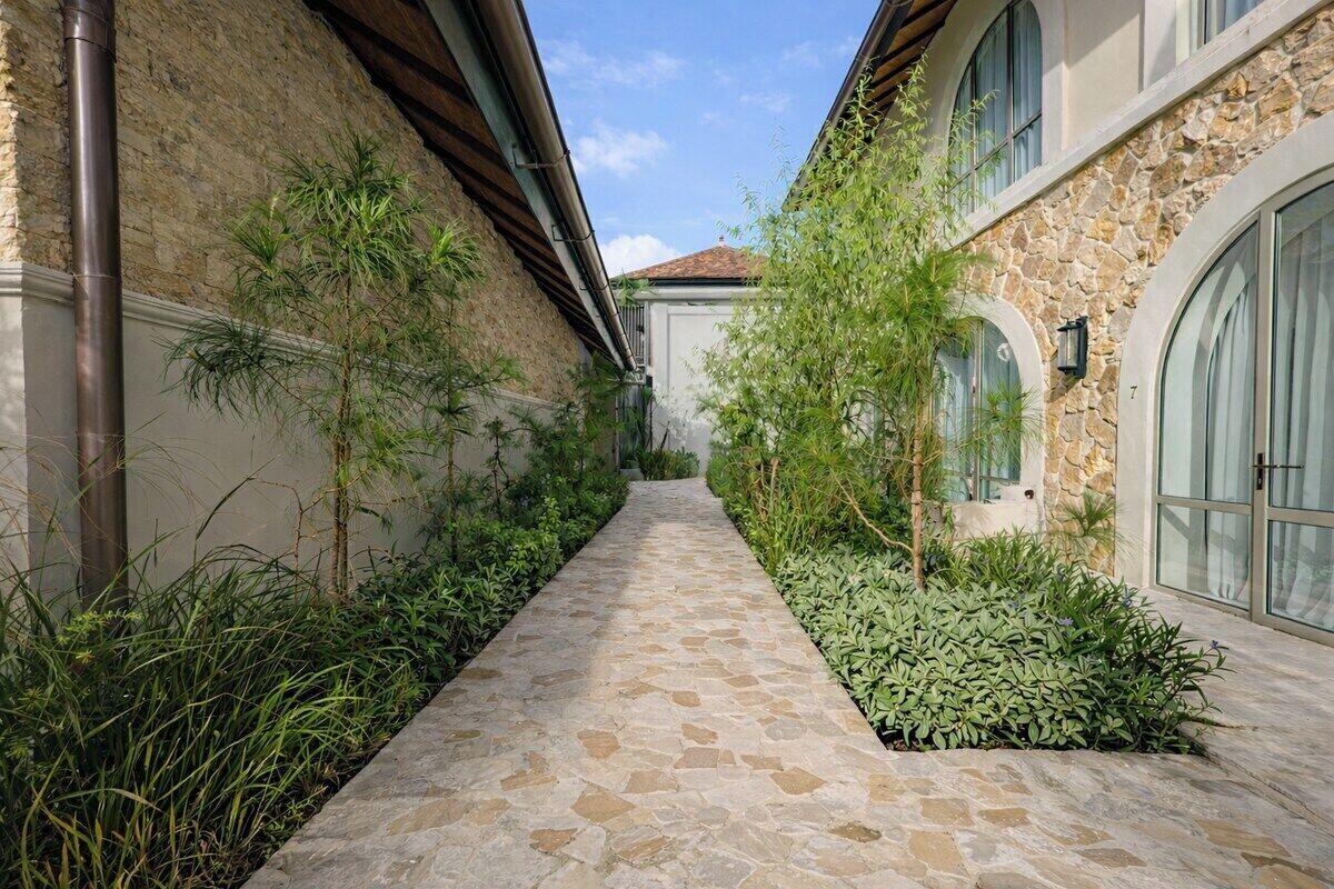 Un sentiero in pietra costeggiato da vegetazione lussureggiante e un edificio in pietra con finestre ad arco.