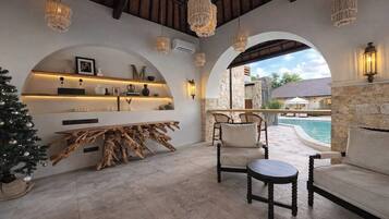 A cozy indoor seating area with a stone fireplace, a wooden coffee table, and a view of a pool.
