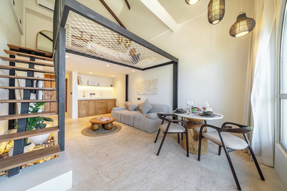 A modern living room with a staircase, a dining area, and a kitchen in the background.