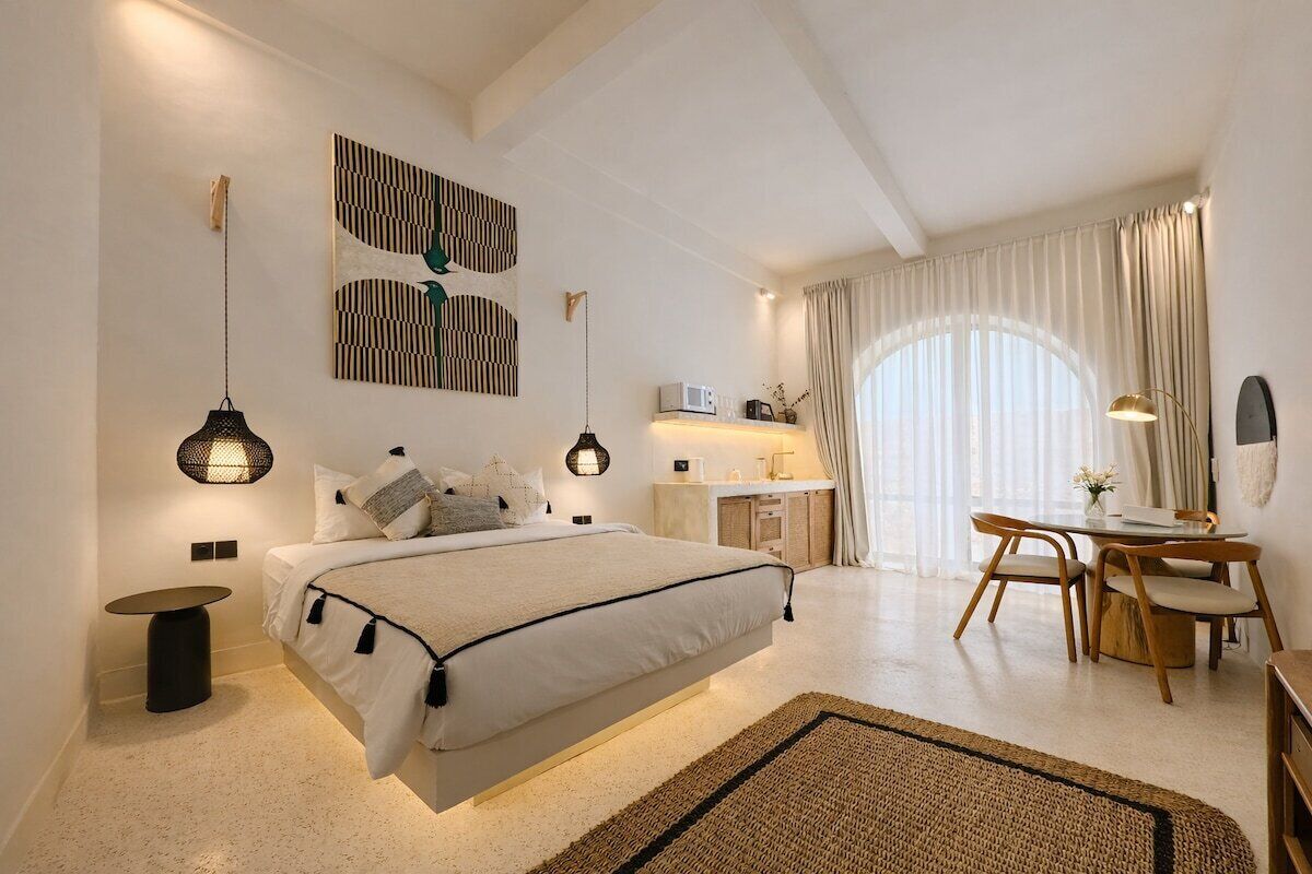 A modern bedroom with a bed, bedside tables, a desk, and a dining area.