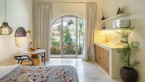 Habitación de hotel con cama, una mesa de comedor con un frutero, una planta en maceta y vistas al exterior a través de un ventanal grande.