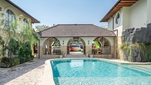 Una piscina con un camino de piedra que lleva a un porche cubierto con mobiliario exterior.