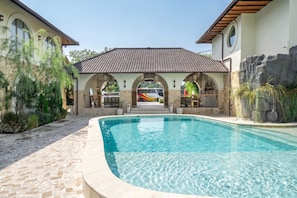 Piscina com caminho de pedra que leva a um alpendre coberto com área de estar ao ar livre.