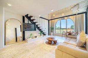 Uma sala de estar moderna com escada, televisão de tela plana, sofá e área de jantar com luz natural.