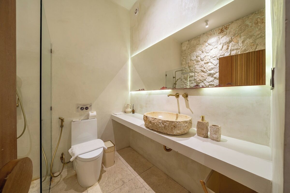 A modern bathroom with a stone sink, a toilet, and a shower area.