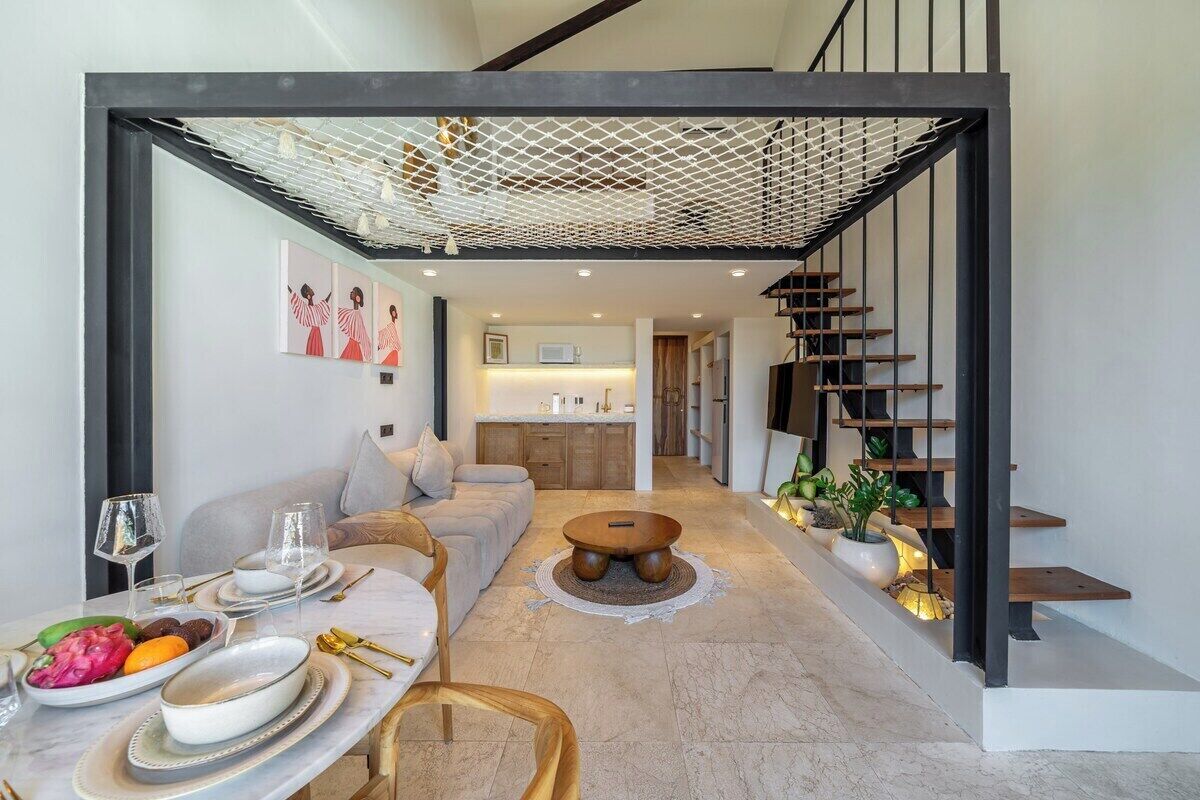 Un interior moderno con comedor, sofá, escalera y cocina al fondo.