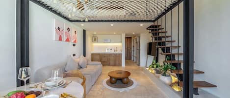 Un interior modern amb zona de menjador, sofà, escala i cuina al fons.