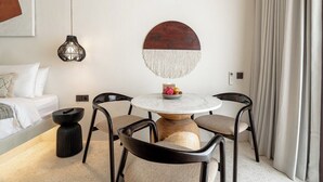 Ein modernes Hotelzimmer mit einem runden Esstisch, schwarzen Stühlen, einem weißen Sofa, einem schwarzen Beistelltisch und einem dekorativen Wandbild.