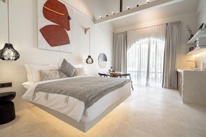 Quarto moderno com cama suspensa, espelho redondo, mesinha e uma janela grande com cortinas.