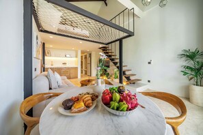 A dining area with a round table, two plates of food, and a staircase leading to an upper level. - Boho Two-Storey Flat Next to Sanur Beach w Bathtub (Kota Denpasar)