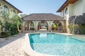 Piscina com caminho de pedra que leva a um alpendre coberto com área de estar ao ar livre.