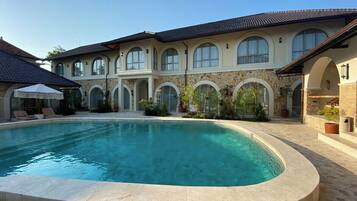 A poolside view of a house with a swimming pool, stone arches, and a covered patio area.