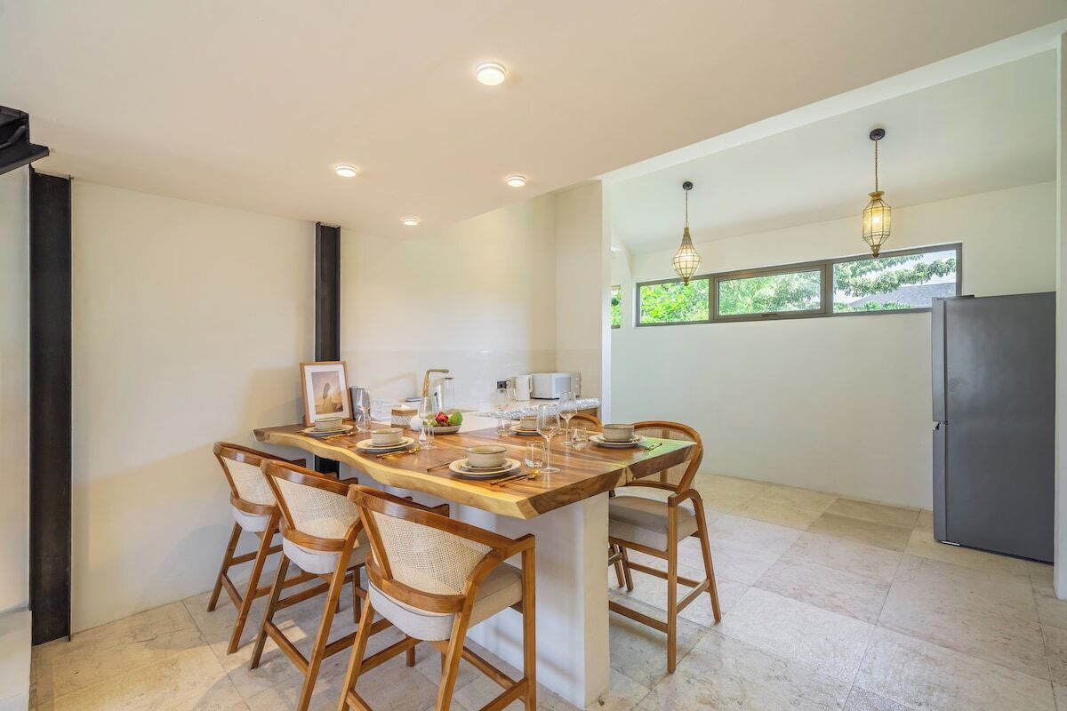 A modern kitchen with a dining area, featuring a wooden table and chairs, a refrigerator, and pendant lighting.