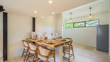 A modern kitchen with a dining area, featuring a wooden table and chairs, a refrigerator, and pendant lighting.