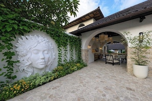 Ein Innenhof mit Steinboden, einer weißen Wand mit Reliefgestaltung und einem Essbereich mit Stühlen und Tisch.