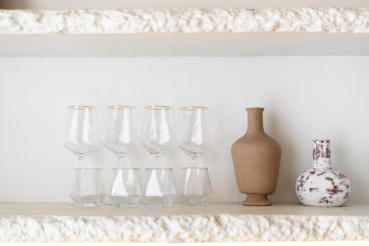 A shelf with five clear glass vases and two ceramic vases.