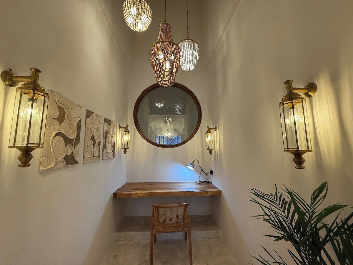A hallway with a wooden desk, a chair, a mirror, and wall-mounted lights.