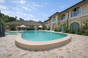 A pool area with a curved edge, lounge chairs, and a building with arched windows and stone walls. - Chic 2BR Villa by Sanur Beach w Pool +Room Jacuzzi (Kota Denpasar)