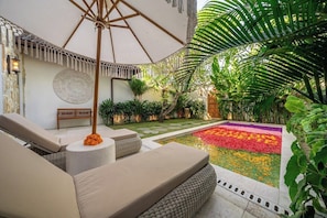 Un patio con piscina, zona de descanso y plantas tropicales.