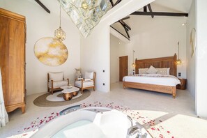 Een slaapkamer met een groot bed, een zithoek met stoelen, een houten garderobe en een badkuip met rozenblaadjes.