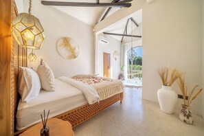 A bedroom with a bed, a hanging light fixture, a vase with dried plants, and a view of the outdoors. - Chic 2BR Villa by Sanur Beach w Pool +Room Jacuzzi (Kota Denpasar)