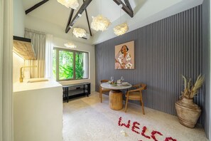 A modern interior with a dining area, a large window, and a decorative welcome mat. - Cozy 1BR Villa w Patio, Pool & Beach in 5 min Walk (Kota Denpasar)