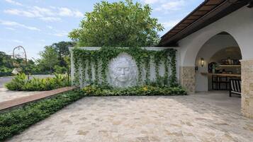A stone-paved entrance with a decorative wall featuring a carved face and greenery.
