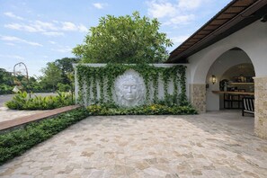 A stone-paved entrance with a decorative wall featuring a carved face and greenery. - Cozy 1BR Villa w Patio, Pool & Beach in 5 min Walk (Kota Denpasar)