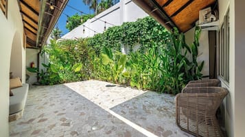 A covered outdoor area with a stone floor, a wicker chair, and lush greenery.