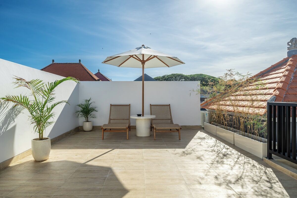 A patio with two wicker chairs, a round table, and a large umbrella.