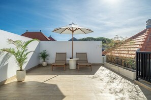 A patio with two wicker chairs, a round table, and a large umbrella. - Cozy 2BR in Sanur w Pool, Rooftop & Beach Access (Kota Denpasar)