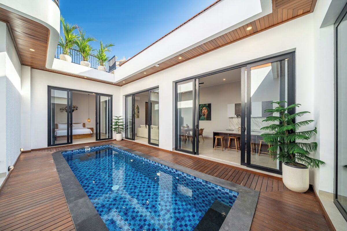 Un espace piscine extérieur moderne, doté d’une terrasse en bois, de portes vitrées donnant sur un espace de vie et de plantes en pot.