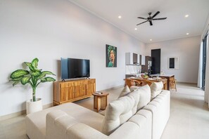 A modern living room with a sofa, TV, and a dining area. - Cozy 2BR in Sanur w Pool, Rooftop & Beach Access (Kota Denpasar)