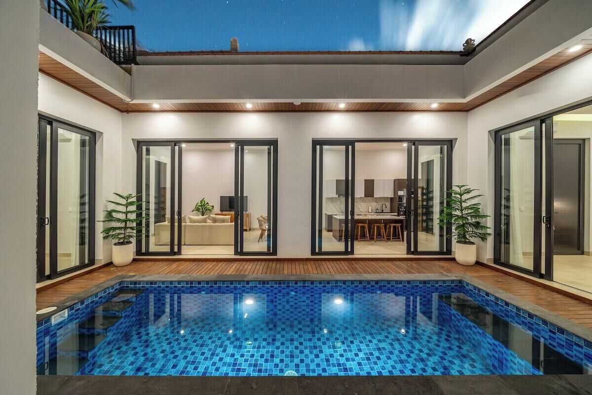 Una casa moderna amb piscina, portes corredisses de vidre i zona de menjador.