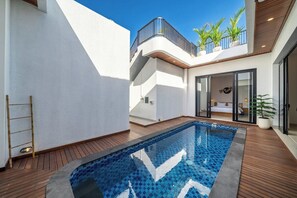 Ein moderner Poolbereich im Freien mit Holzterrasse, Glastür und einem Balkon mit Topfpflanzen.