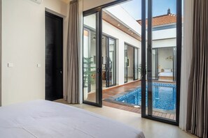 Ein Schlafzimmer mit einem großen Bett und bodentiefen Glasfenstern, die zu einem Poolbereich führen.